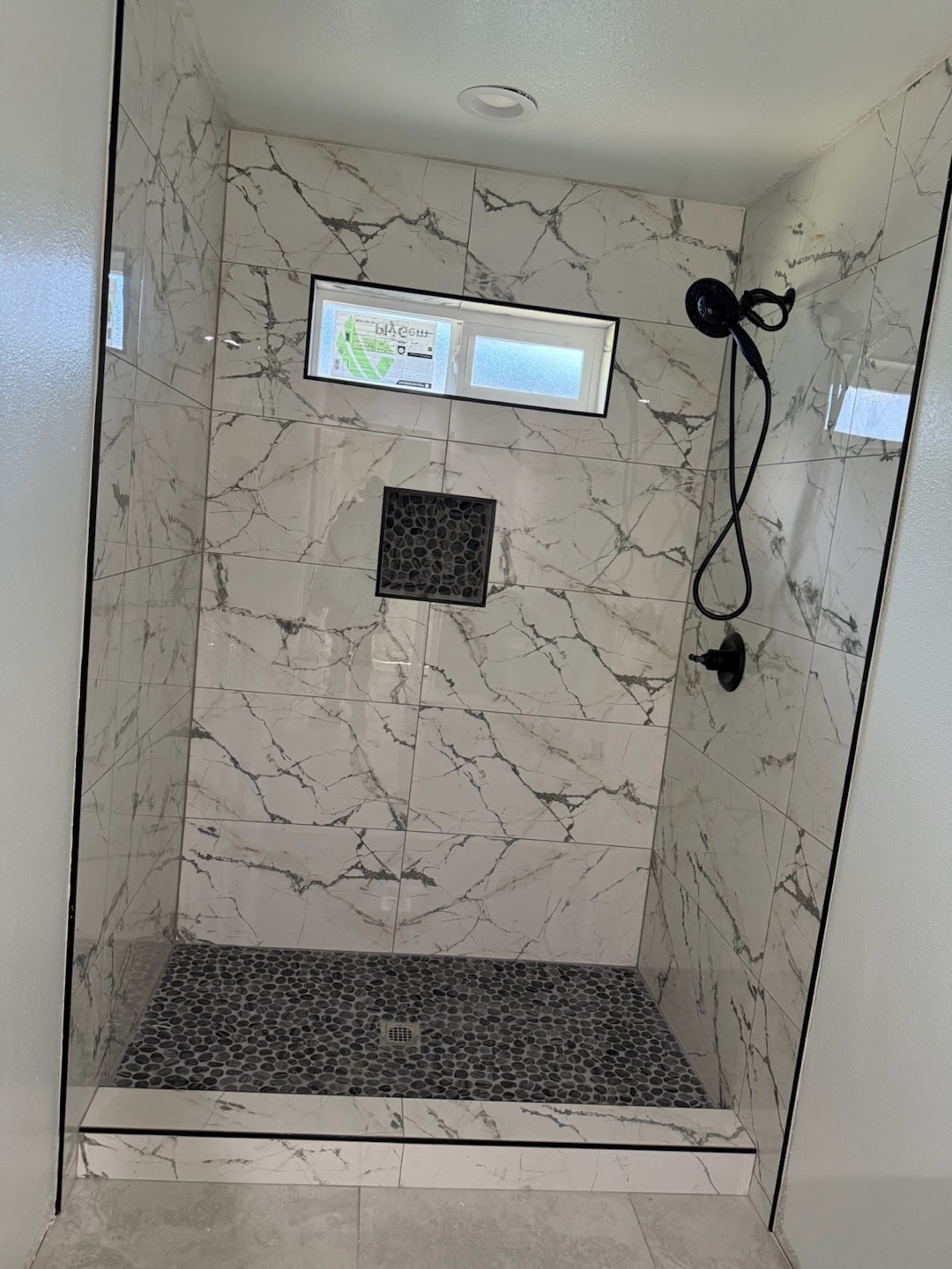 Finished marble shower with recessed niche and pebble floor